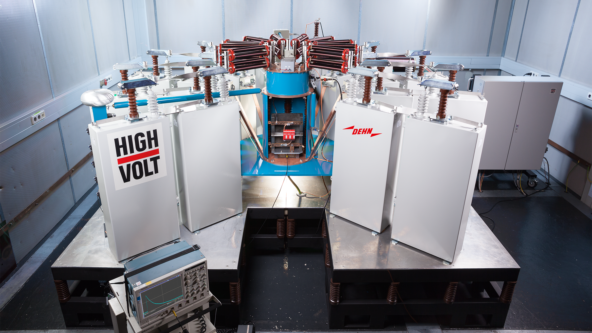 High-voltage testing apparatus with multiple insulated compartments and a central, blue-and-red component, situated in a laboratory setting.