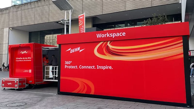 A red mobile workspace display with the word 'Workspace' and the DEHN logo. The display features a slogan: '360° Protect. Connect. Inspire.' A truck is parked next to the display.