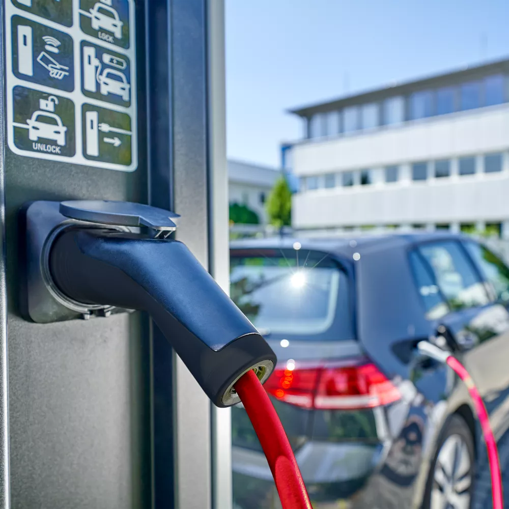 Electric vehicle charging station with a red charging cable connected to a dark gray car.